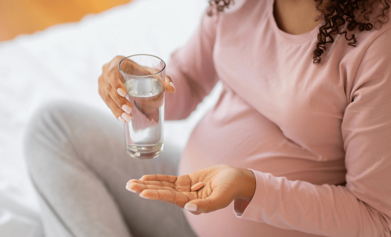 Pregnant woman holding a glass of water and a vitamin pill, emphasizing prenatal nutrition.