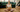 A serene pregnant woman practicing prenatal yoga in a cozy living room. She sits cross-legged on a rug, cradling her baby bump with both hands while meditating.