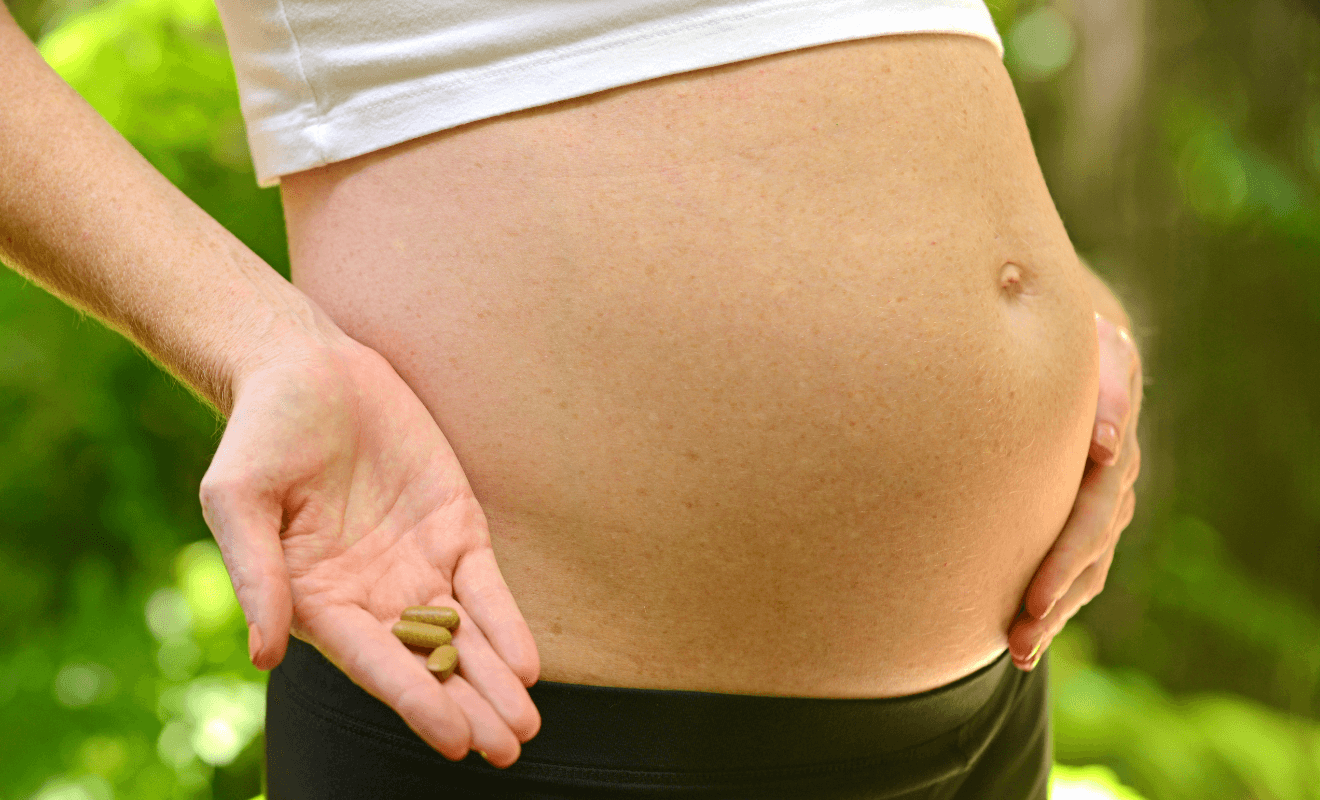 Pregnant woman holding prenatal vitamin capsules next to her belly, illustrating choosing the best prenatal vitamins for a healthy pregnancy.