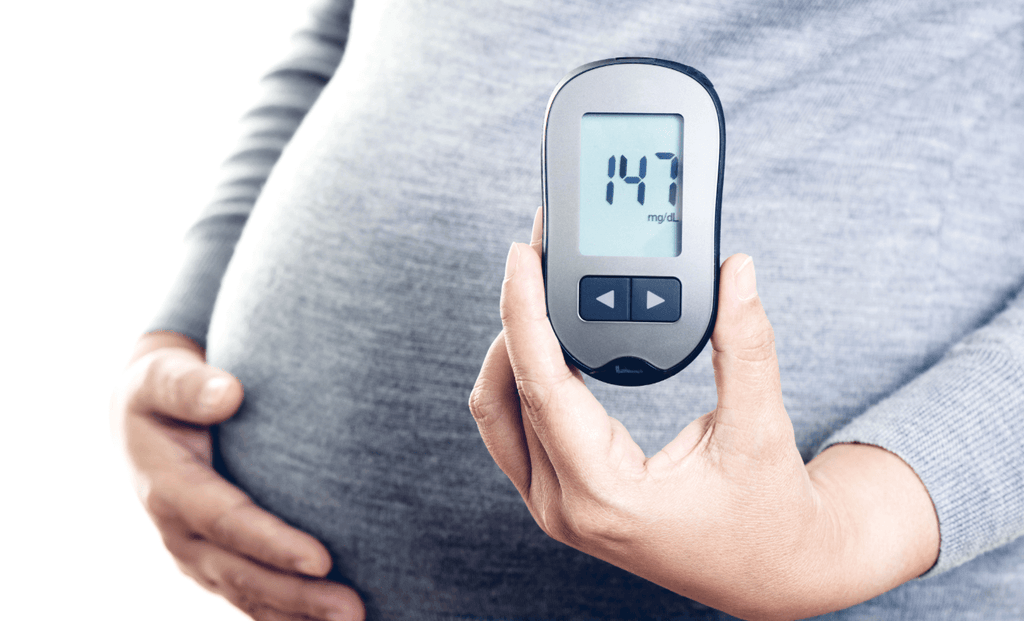 Pregnant woman holding a blood glucose meter displaying a reading of 147 mg/dL, indicating blood sugar management.