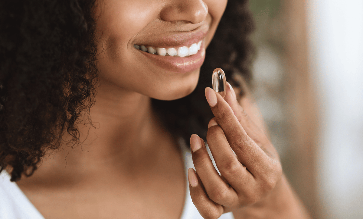 Smiling woman holding a clear softgel supplement between her fingers