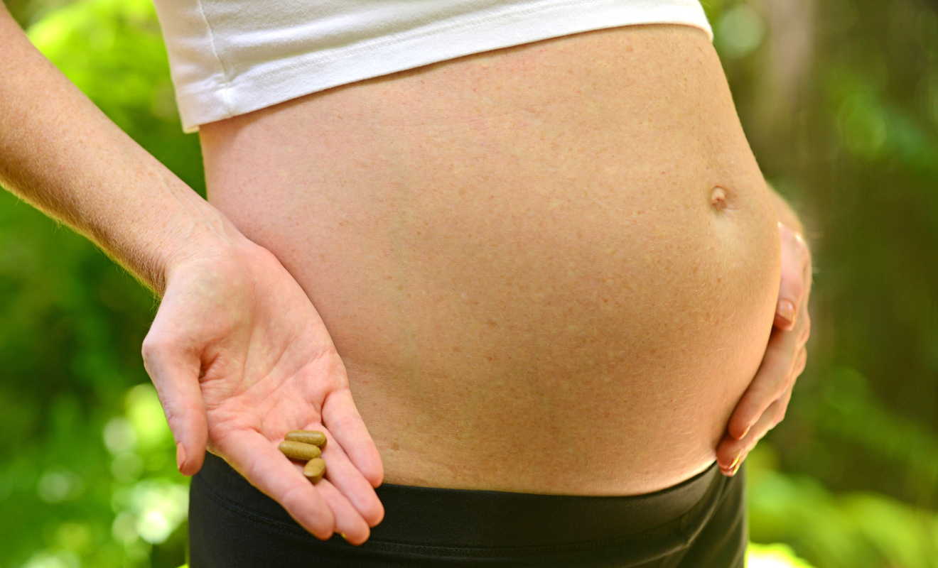 Pregnant woman holding prenatal vitamin capsules next to her belly, illustrating choosing the best prenatal vitamins for a healthy pregnancy.