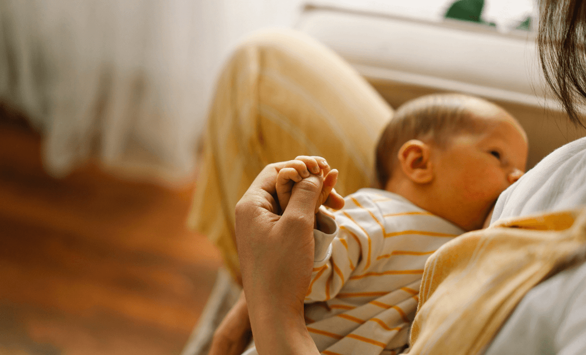 Mother breastfeeding newborn while holding baby’s hand, managing breastfeeding pain and discomfort naturally.