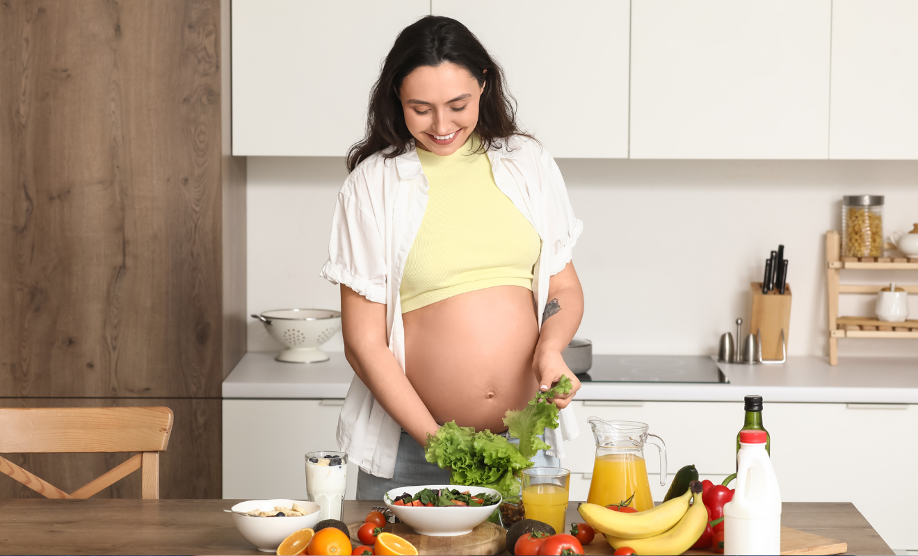 Smiling pregnant woman preparing a healthy green salad in her kitchen, representing a balanced pregnancy diet plan.