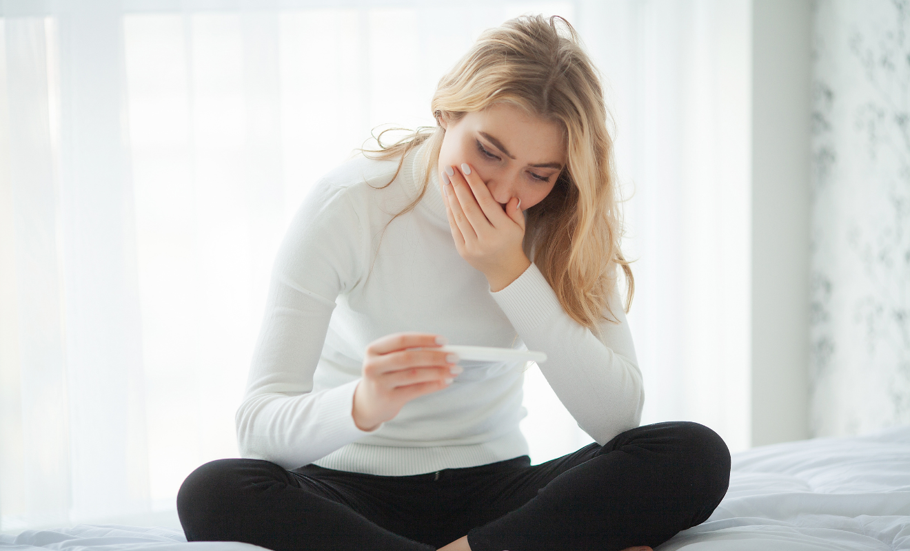 A woman looking surprised and emotional while holding a positive pregnancy test, representing early pregnancy symptoms and the first signs.