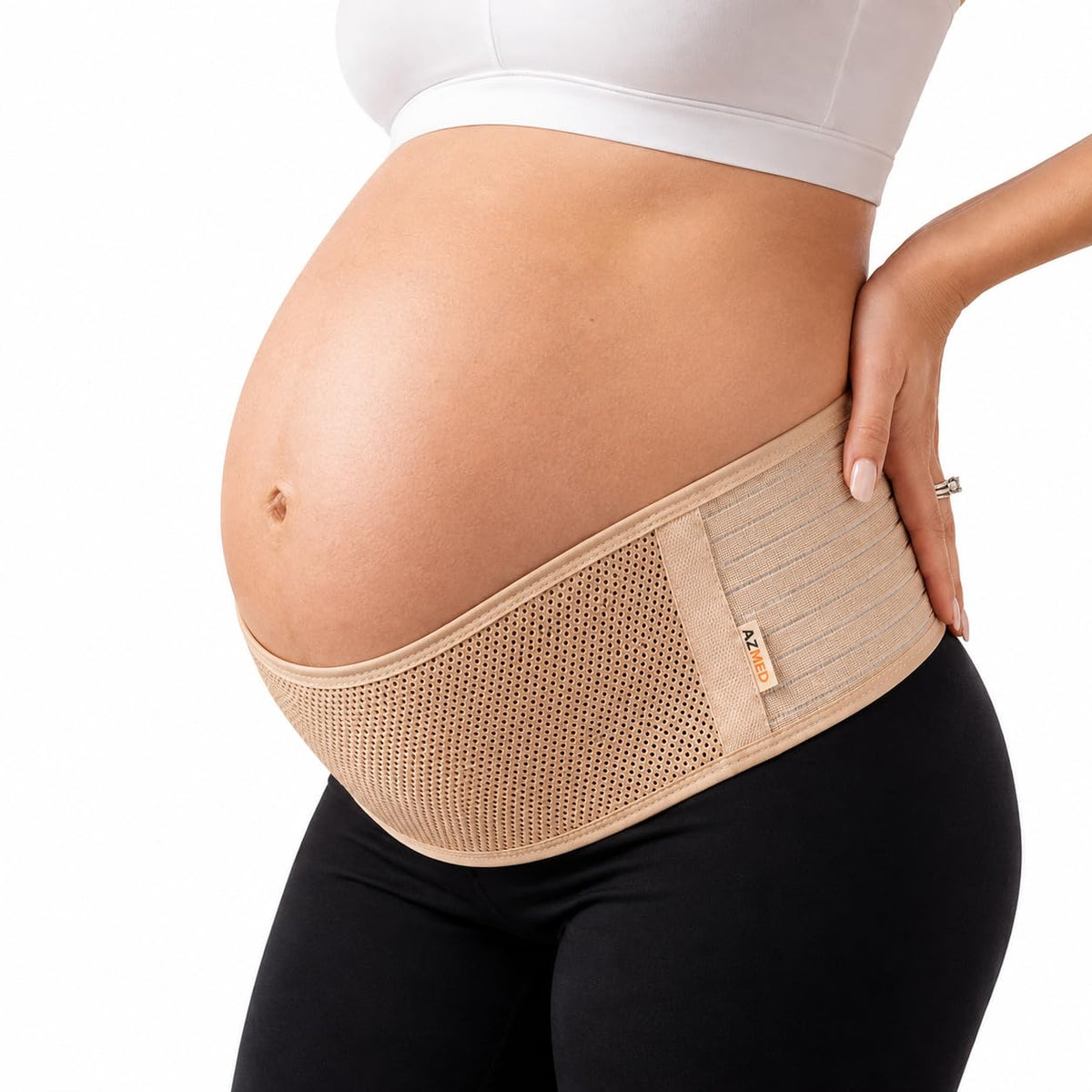 The AZMED maternity support belt in beige, worn under the bump and wrapped low across the hips, with the wearer's hand on her lower back.