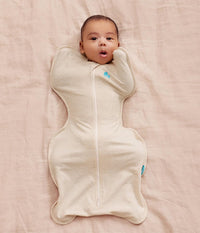 Newborn resting arms-up in the oatmeal Swaddle Up swaddle