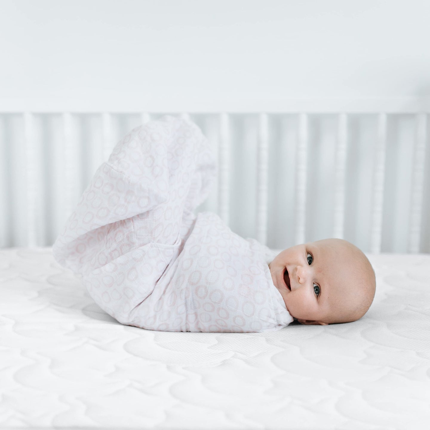 Happy baby swaddled in a soft blanket, lying on a crib mattress, enjoying a cozy sleep.