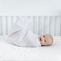 Happy baby swaddled in a soft blanket, lying on a crib mattress, enjoying a cozy sleep.