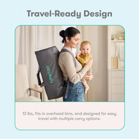 Parent carrying the Newton Compact travel crib as a backpack while holding a baby