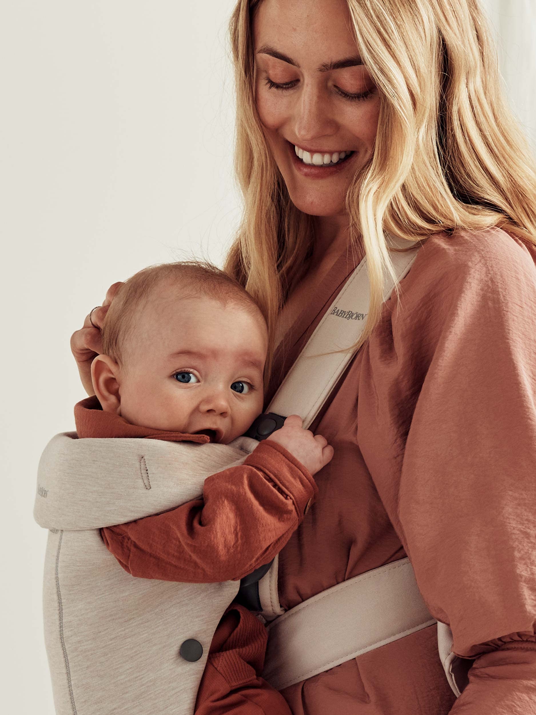 Mother smiling while carrying her baby in a BabyBjörn Mini baby carrier, showcasing comfort and closeness.