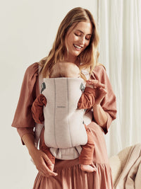 Mother wearing a newborn baby carrier with a smiling baby, showcasing the BabyBjörn Mini baby carrier.