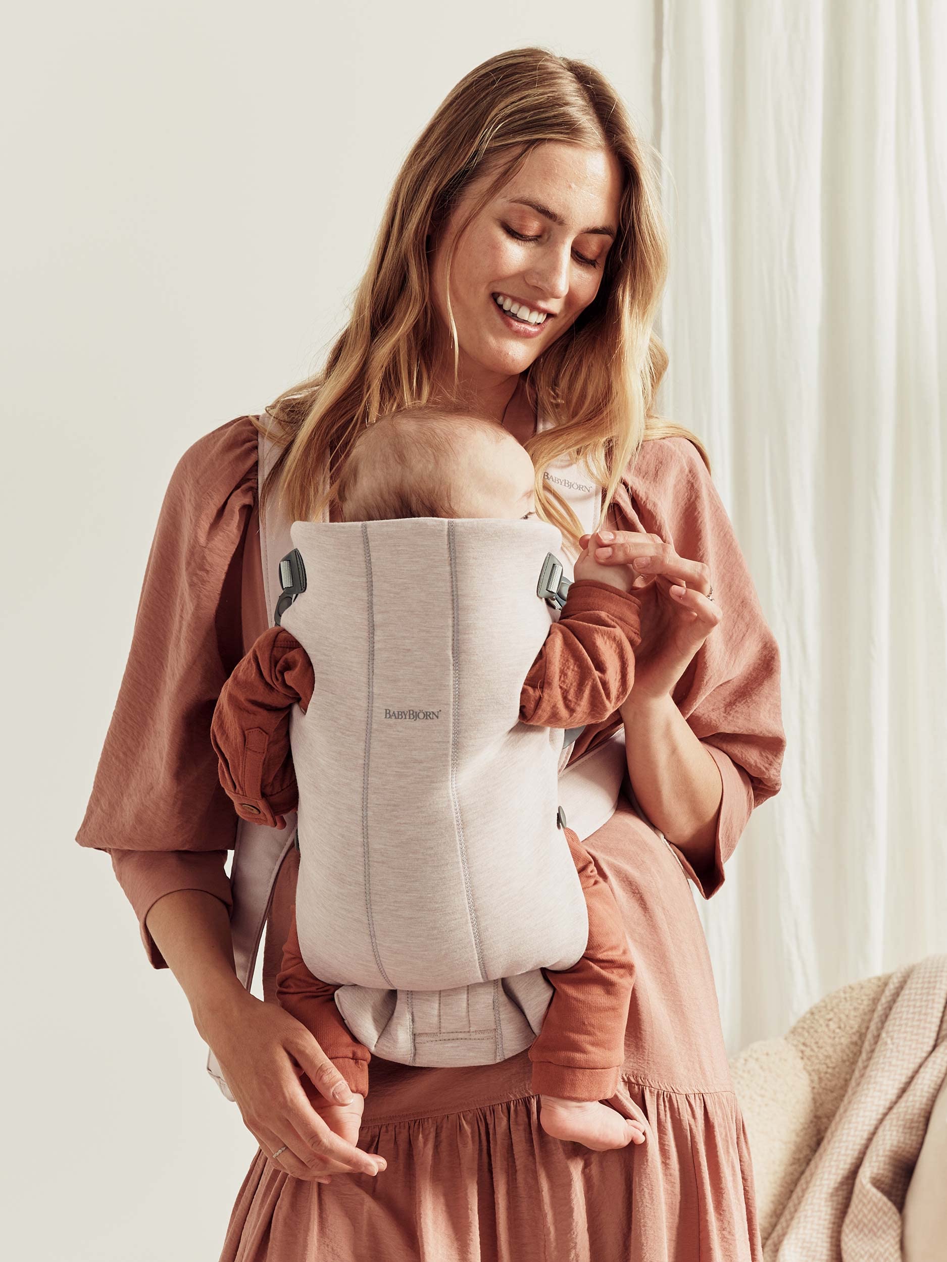 Mother wearing a newborn baby carrier with a smiling baby, showcasing the BabyBjörn Mini baby carrier.