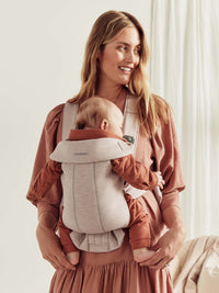 A woman holds her baby in a BabyBjörn Mini Baby Carrier, showcasing comfort and ease for parents with newborns.