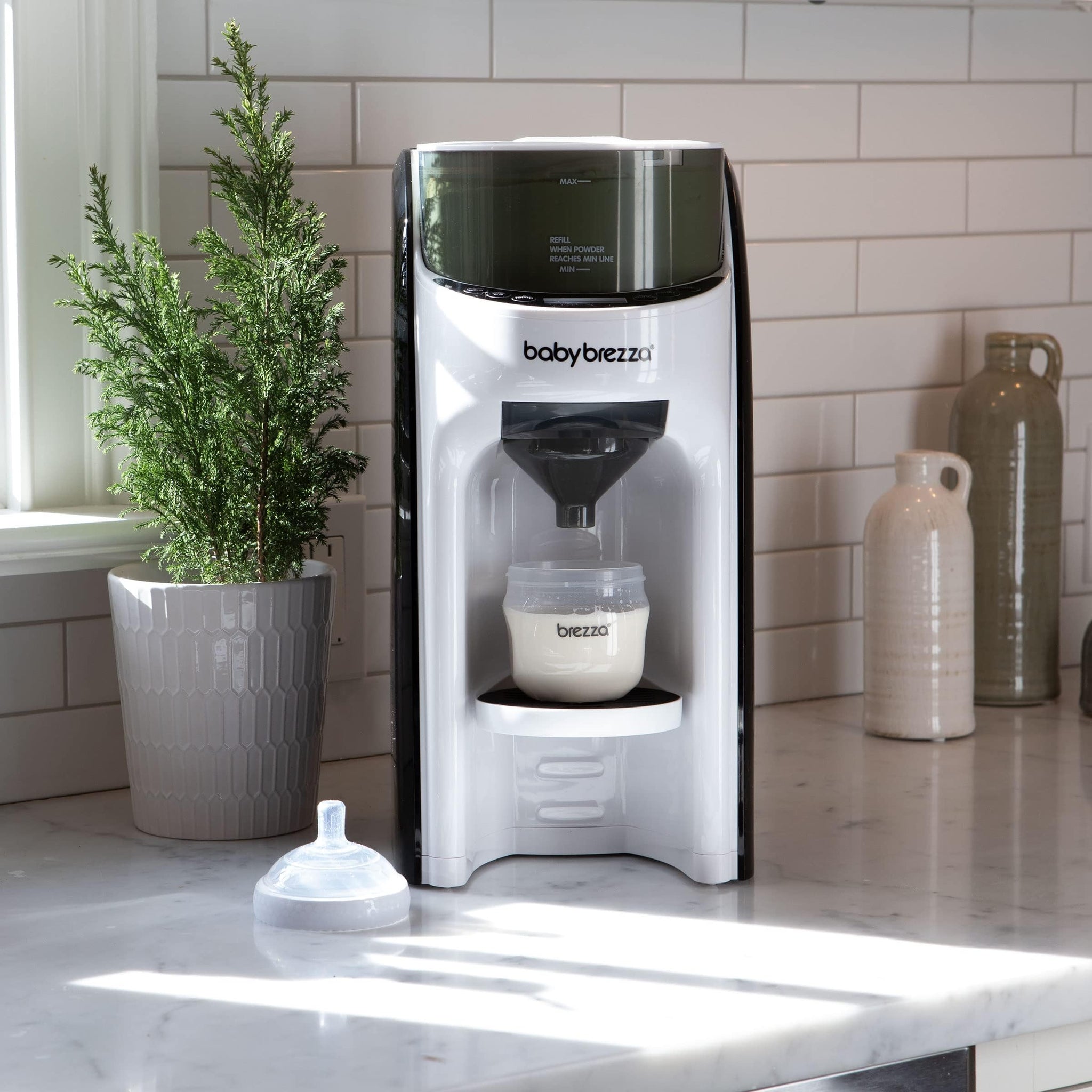 Automatic formula dispenser for newborns on a kitchen counter with bottles and a plant.