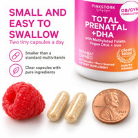 Two small Pink Stork prenatal vitamin capsules next to a penny and a raspberry, showing the capsule size
