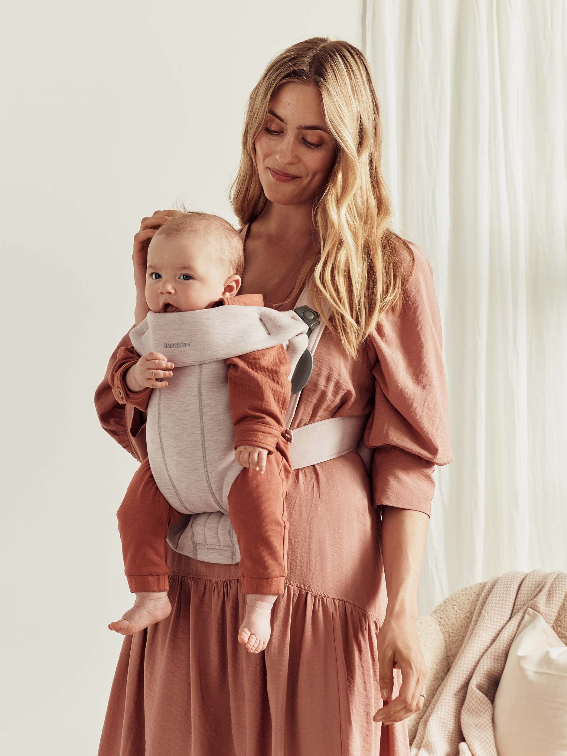 Mom using a baby carrier to hold her newborn comfortably while dressed in a stylish outfit.