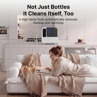 Momcozy D8 bottle washer on a kitchen counter beside the sink, advertising its self-clean mode