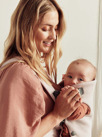 Woman holding her baby in a baby carrier, showcasing the BabyBjörn Mini newborn carrier for comfort and closeness.