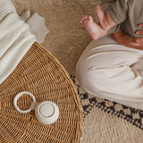 Portable sound machine for baby on a woven table, with a parent and infant relaxing nearby.