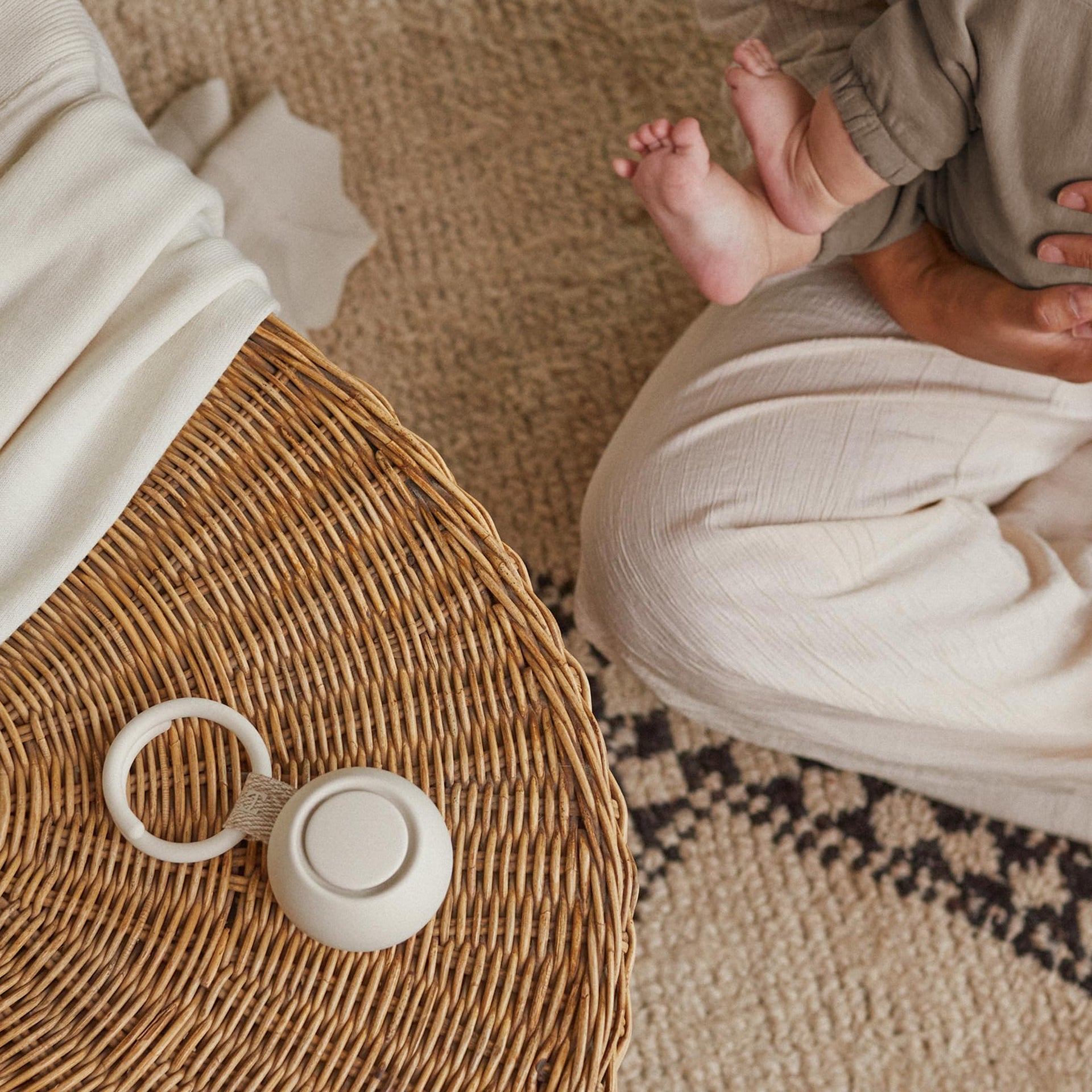 Portable sound machine for baby on a woven table, with a parent and infant relaxing nearby.