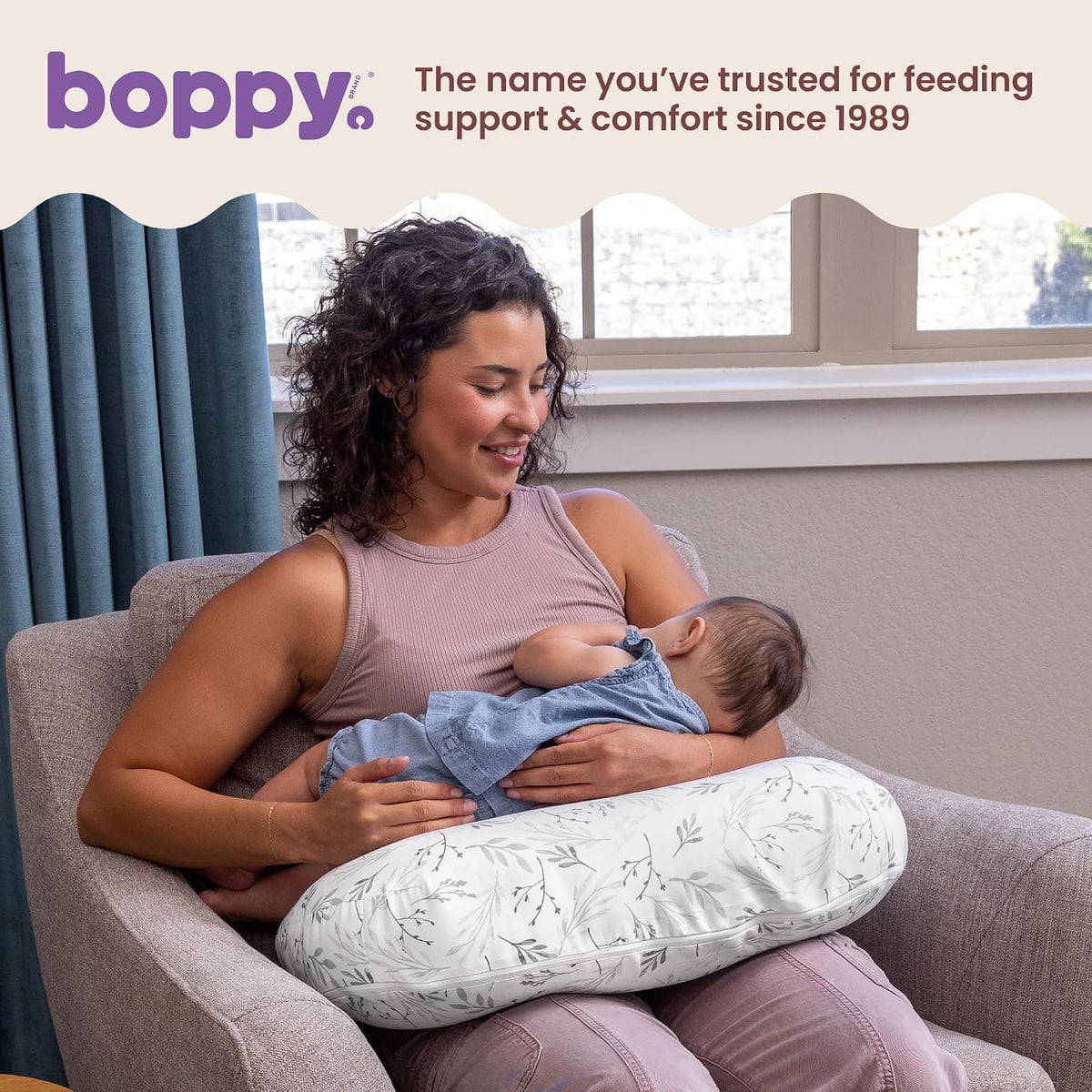 Mother breastfeeding in an armchair using the Boppy pillow, with Boppy's line that it has been trusted for feeding support since 1989.
