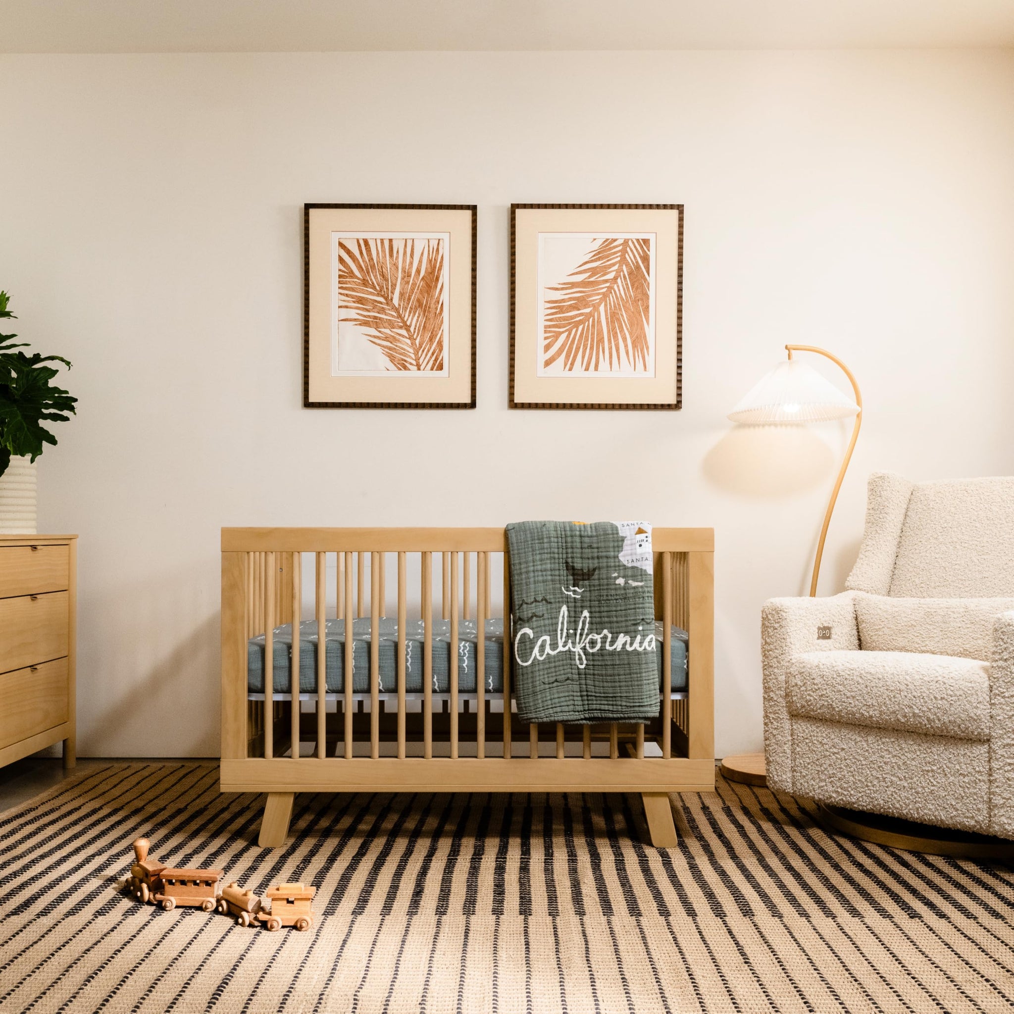 Convertible crib in a modern nursery with warm wood finish and decorative wall art.