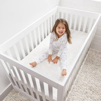 Happy child sitting on HALO DreamWeave breathable crib mattress in a white crib, showcasing comfort and safety for sleep.