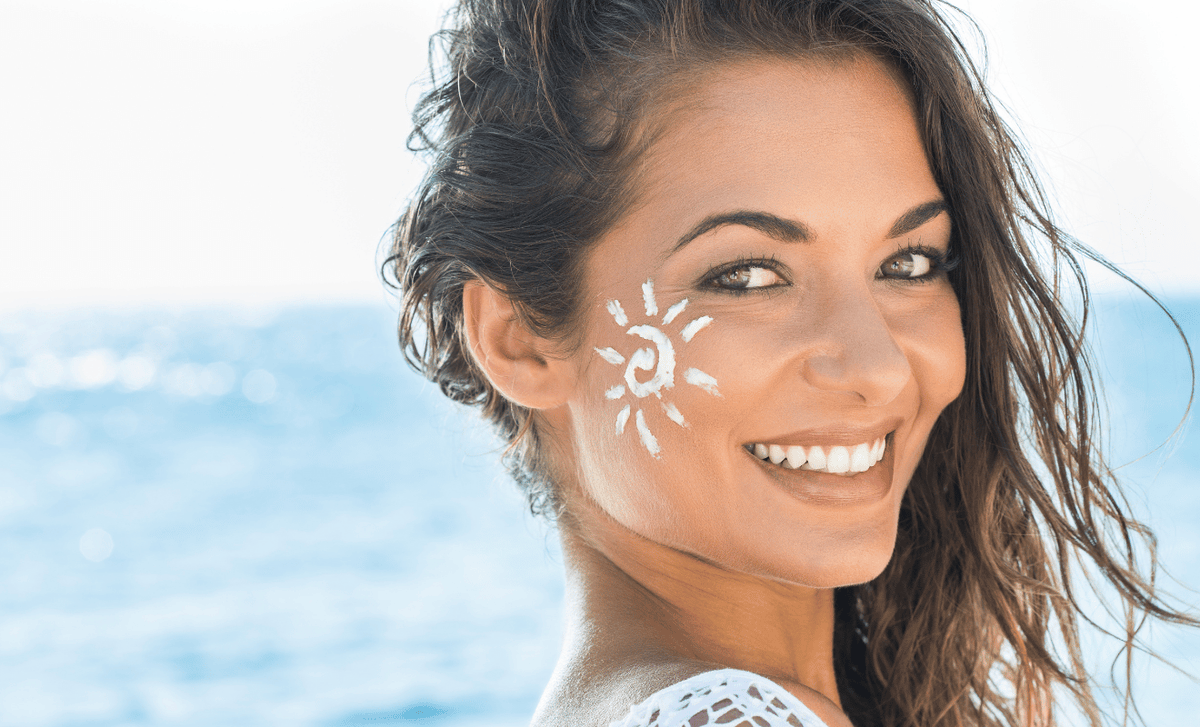 Smiling woman at the beach with a sun drawn in white sunscreen on her cheek